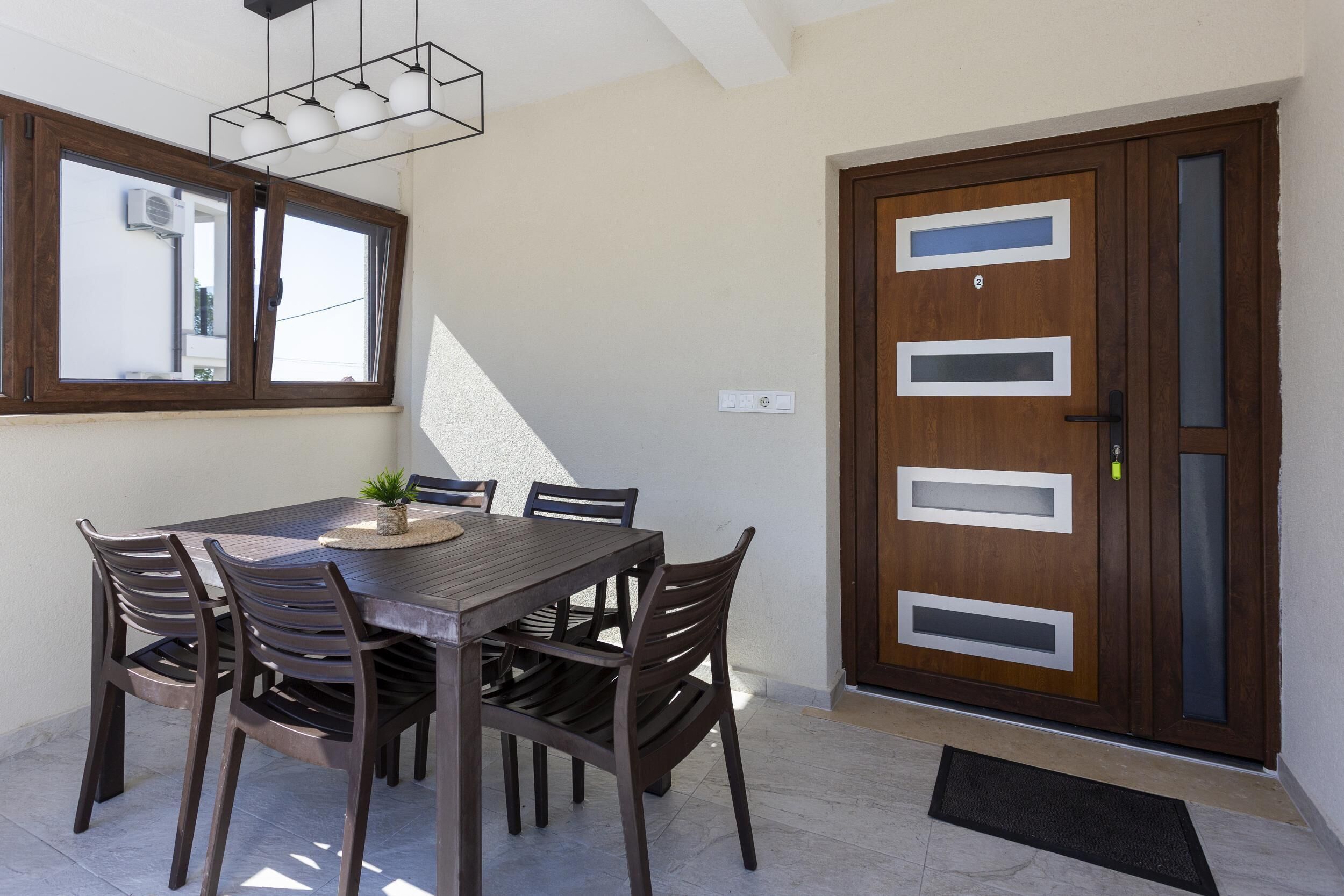 A dining area with a wooden table and chairs, a potted plant, and a modern door with frosted glass panels.