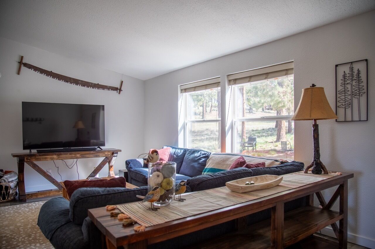 A living room with a TV, sofa, coffee table, and a window with a view of the outdoors.