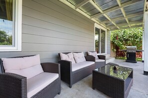 Une terrasse couverte, aménagée avec des meubles en osier et une table à plateau en verre.