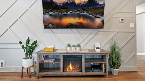 Ein Wohnzimmer mit Kamin, einem Wand-Fernseher, der eine Berglandschaft zeigt, und einem Bücherregal mit Büchern.