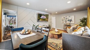 Ein modernes Wohnzimmer mit Essbereich, ausgestattet mit einem großen Flachbildfernseher, einem Sofa, einem Couchtisch und einem Esstisch mit Stühlen.
