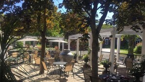 An outdoor patio area with tables and chairs, surrounded by trees and umbrellas.
