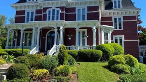 A large, stately Victorian-style house with a prominent front porch, multiple windows, and a well-maintained garden.