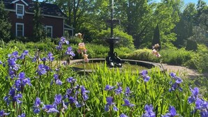 A garden with a fountain, surrounded by lush greenery and purple flowers.