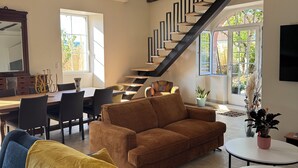 A modern living room with exposed wooden beams, a staircase, a dining area, and a view of the outdoors.