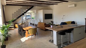 A modern kitchen with a central island, a dining area with a wooden table and chairs, and a staircase leading to an upper level.