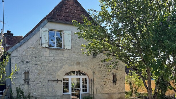 A stone house with a sloped roof, a wooden bench, and a gravel driveway.