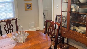 Comedor con mesa de madera, sillas, candelabro, aparador con puertas de cristal y cuadros en la pared.