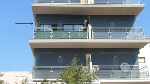 Un edificio de varios pisos con balcones, cielo despejado y una palmera en primer plano.