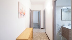 A hallway with a wooden bench, a framed picture on the wall, and a bathroom with a sink and mirror. - Spacious Family Apartment in Pigneto  (Rome)