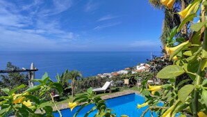 Ein Pool mit Meerblick, umgeben von Grün und einem weißen Sonnenschirm.