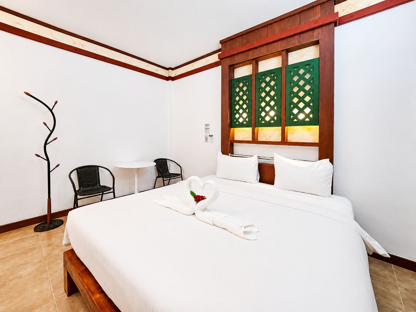 A hotel room with a bed, a desk, two chairs, a coat rack, and a window with green shutters.
