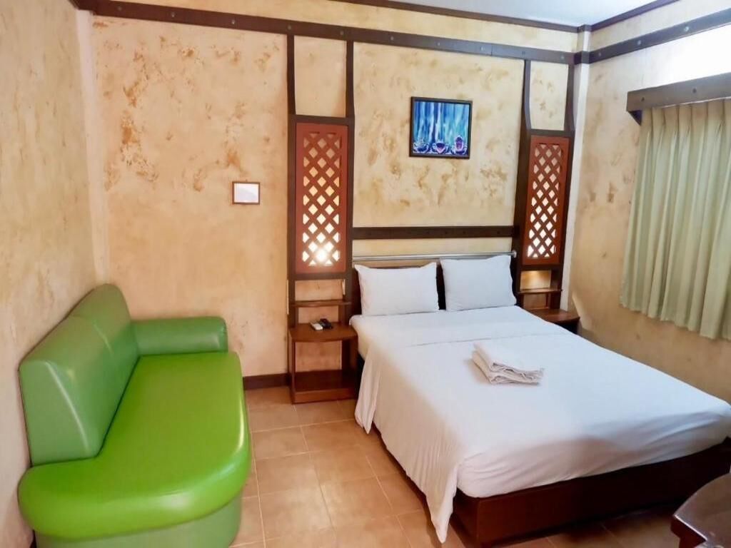 A hotel room with a bed, a green sofa, a nightstand, and a wall-mounted picture.