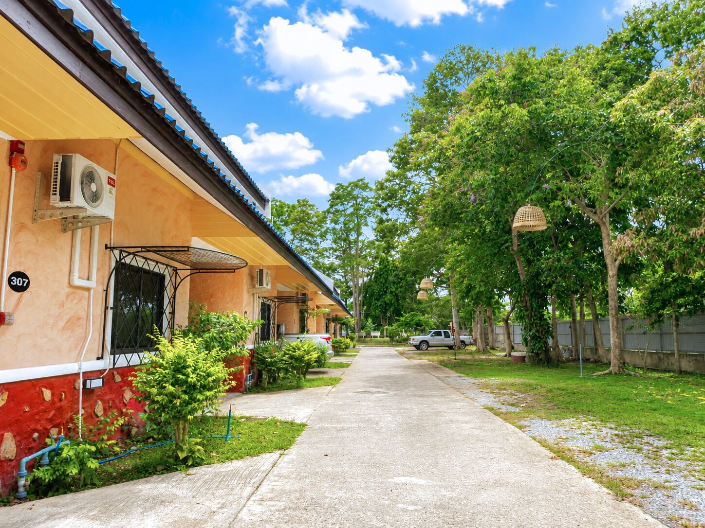 A row of single-story buildings with air conditioning units, a paved walkway, and greenery.