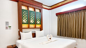 Una habitación de hotel con cama, cabecera de madera, mesita de noche pequeña y ventana con cortinas.