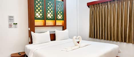 A hotel room with a bed, a wooden headboard, a small bedside table, and a window with curtains.