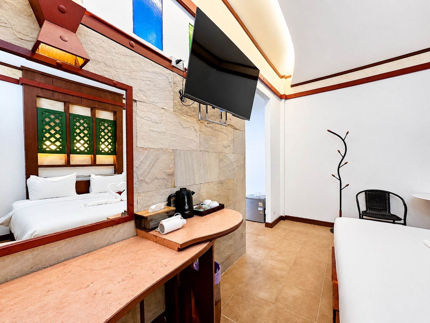 Een moderne badkamer met een stenen muur, een houten wastafelmeubel, een zwarte koffiezetapparaat en een flatscreen televisie die boven de spiegel is bevestigd.