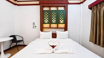 Una habitación de hotel con una cama, una mesita pequeña, una silla y una ventana con marco de madera y paneles de celosía verde.