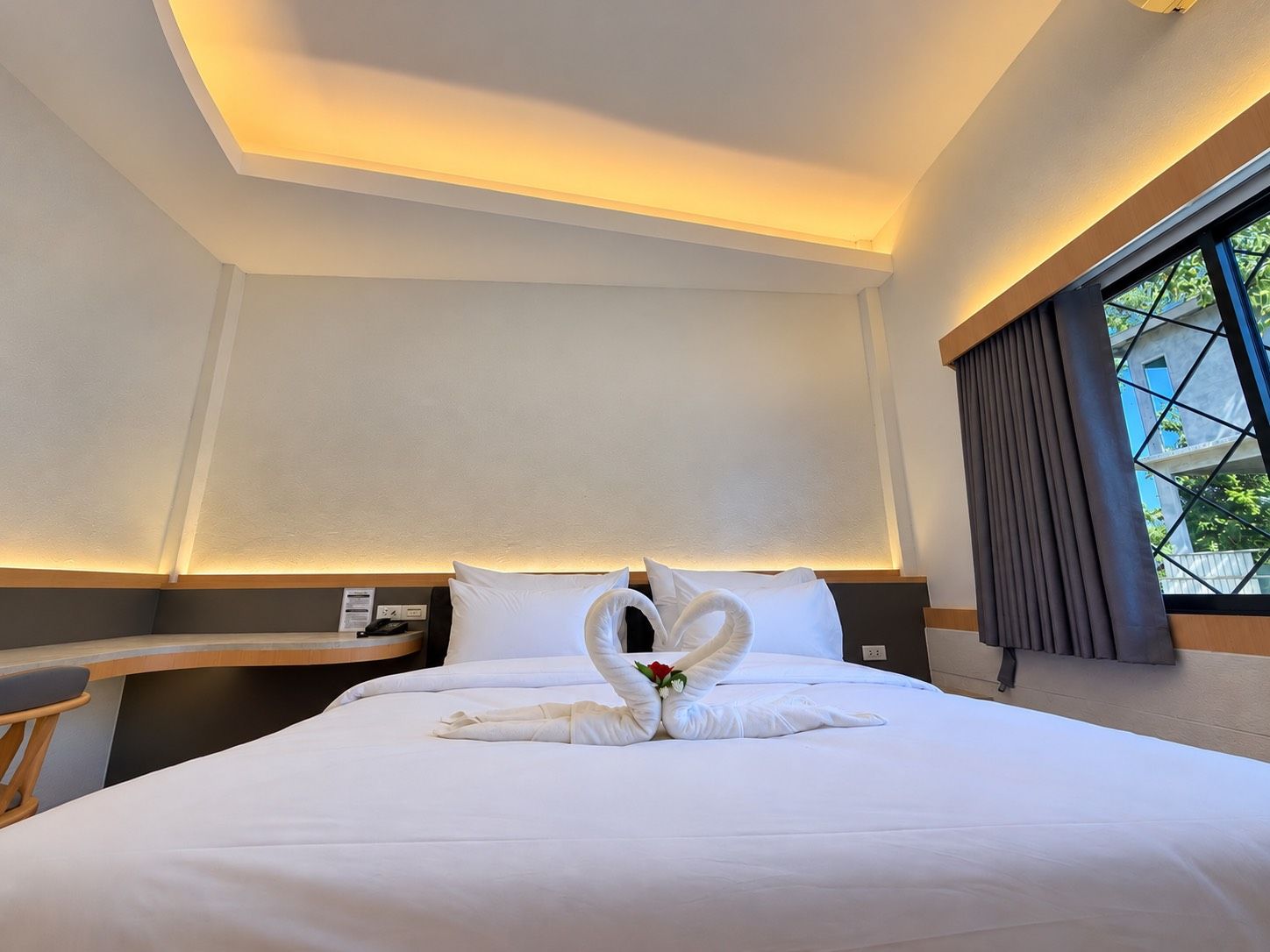 Habitación de hotel con una cama bien hecha, un escritorio y un ventanal con cortinas.