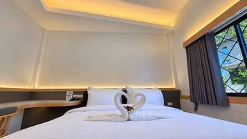 Habitación de hotel con una cama bien hecha, un escritorio y un ventanal con cortinas.