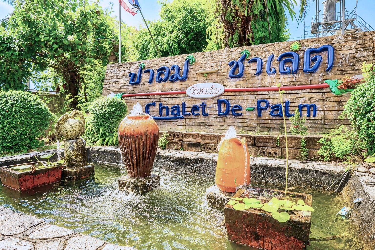 A water feature with a sign reading 'Chalet De Palm' in a garden setting.