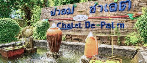 A water feature with a sign reading 'Chalet De Palm' in a garden setting.