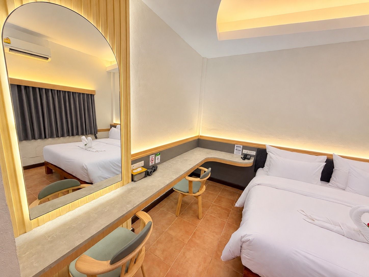 A hotel room with a bed, a desk, a chair, a mirror, and a wall-mounted phone.