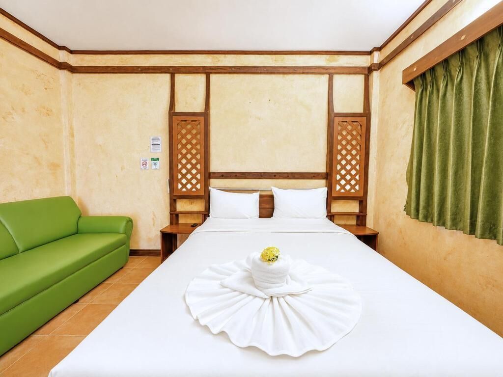 A hotel room with a bed, a green sofa, and a decorative white item on the bed.