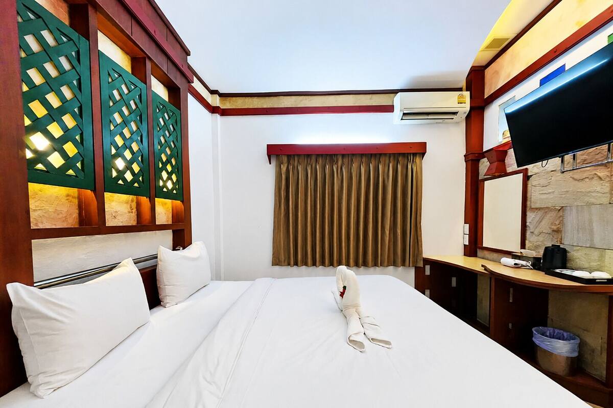 A hotel room with a bed, a desk, a television, and an air conditioning unit.