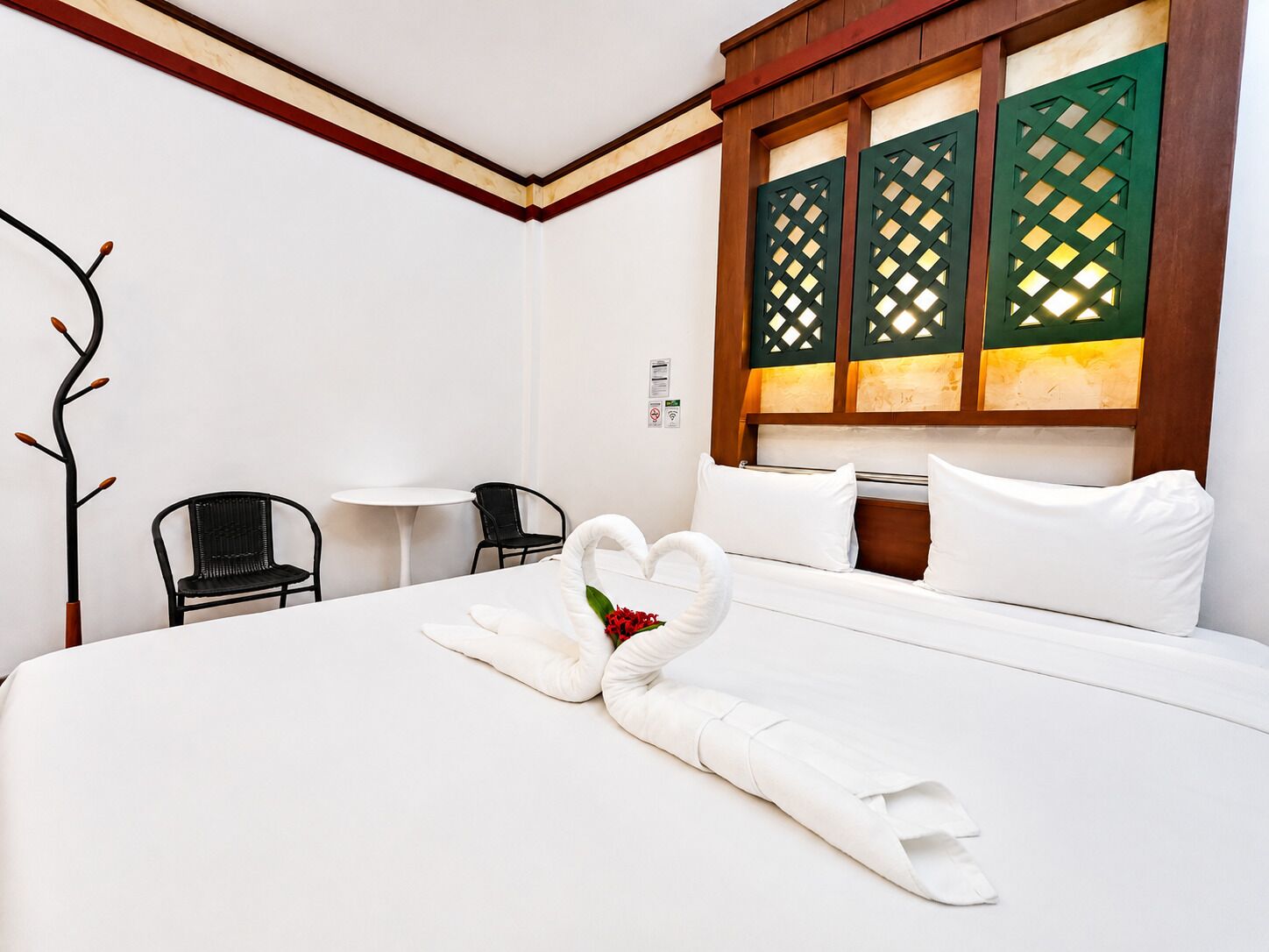A hotel room with a bed, two chairs, a small table, and a decorative wall panel.