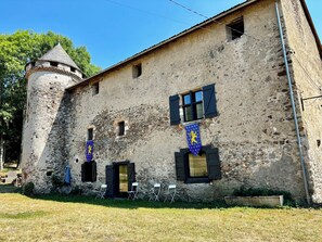 Edificio de piedra histórico con torreta, una bandera y mesas al aire libre.