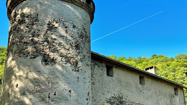 Um edifício histórico de pedra com uma torre redonda, várias janelas e um gramado.