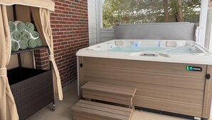 Un bain à remous avec un revêtement extérieur en bois et une étiquette de marque, un mur en briques et un espace de détente couvert avec des coussins.