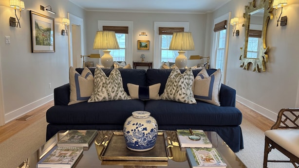Un salon avec un canapé bleu foncé, des coussins décoratifs, une table basse avec des livres et un vase, et des lampes fixées au mur.