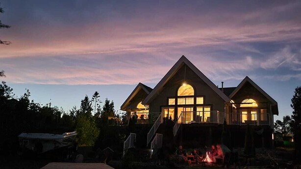 A two-story house with a large central window and a fire pit in the front yard. - Amazing waterfront luxury home in millionaire area only minutes from town (Tobermory)