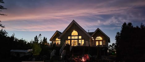 A two-story house with a large central window and a fire pit in the front yard.