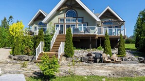 A large, two-story house with a wrap-around porch, a staircase leading to the upper level, and a covered outdoor seating area. - Amazing waterfront luxury home in millionaire area only minutes from town (Tobermory)