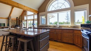 A spacious kitchen with a large island, wooden cabinets, and a stone accent wall. - Amazing waterfront luxury home in millionaire area only minutes from town (Tobermory)