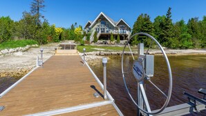 A wooden dock leading to a house with a large front porch and a circular water feature. - Amazing waterfront luxury home in millionaire area only minutes from town (Tobermory)