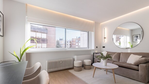 Una sala de estar moderna con un ventanal grande, un espejo redondo, un sofá, una mesa de centro y una planta.