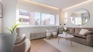 Een moderne woonkamer met een groot raam, een ronde spiegel, een bank, een bijzettafeltje en een plant.