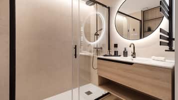 Een moderne badkamer met een douchecabine van glas, een ronde spiegel, een houten wastafel en een witte wasbak.