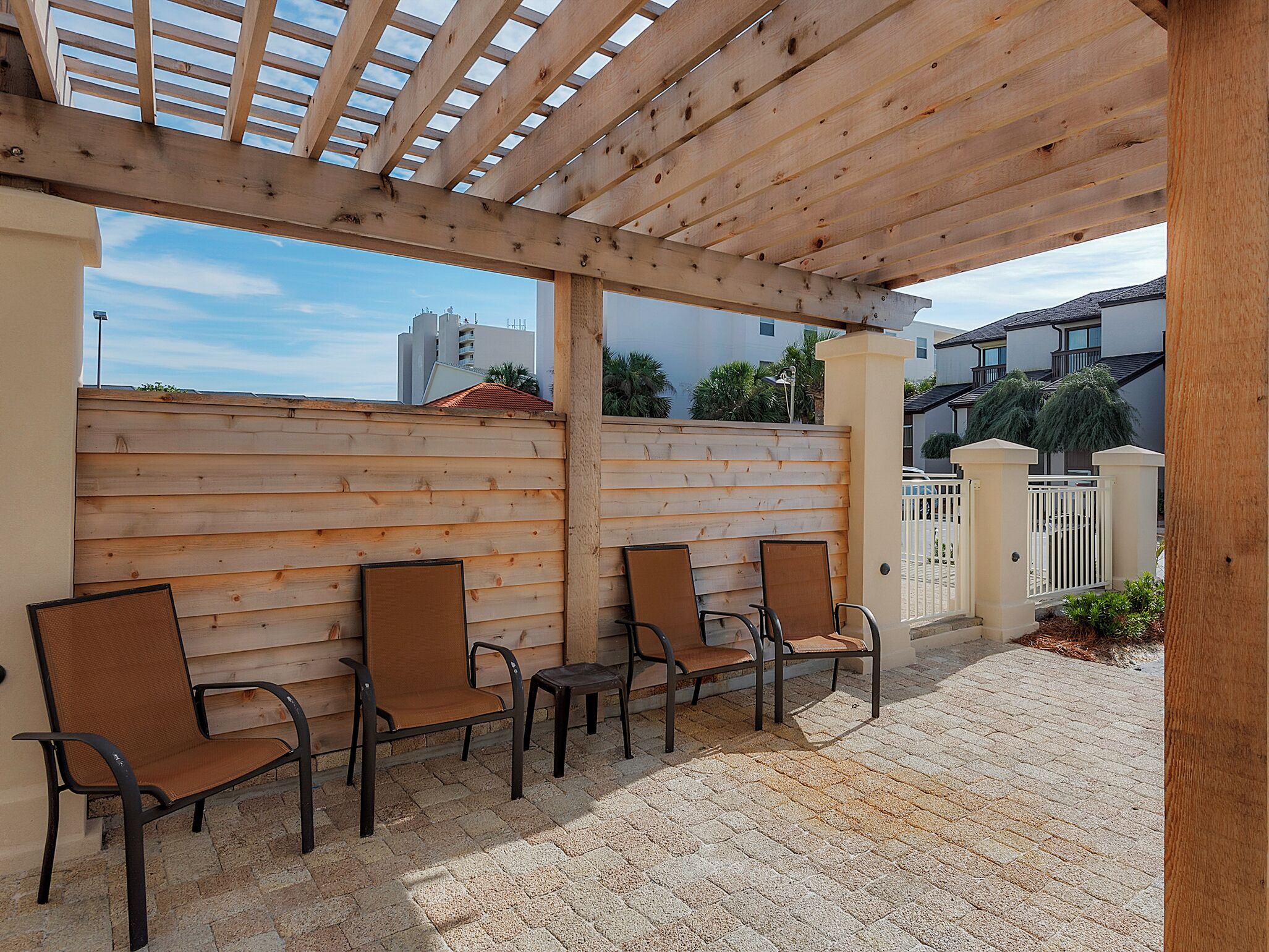 Een terras buiten met houten stoelen en een pergola.