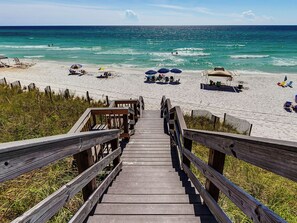 A wooden boardwalk leading to a beach with umbrellas and beach chairs.