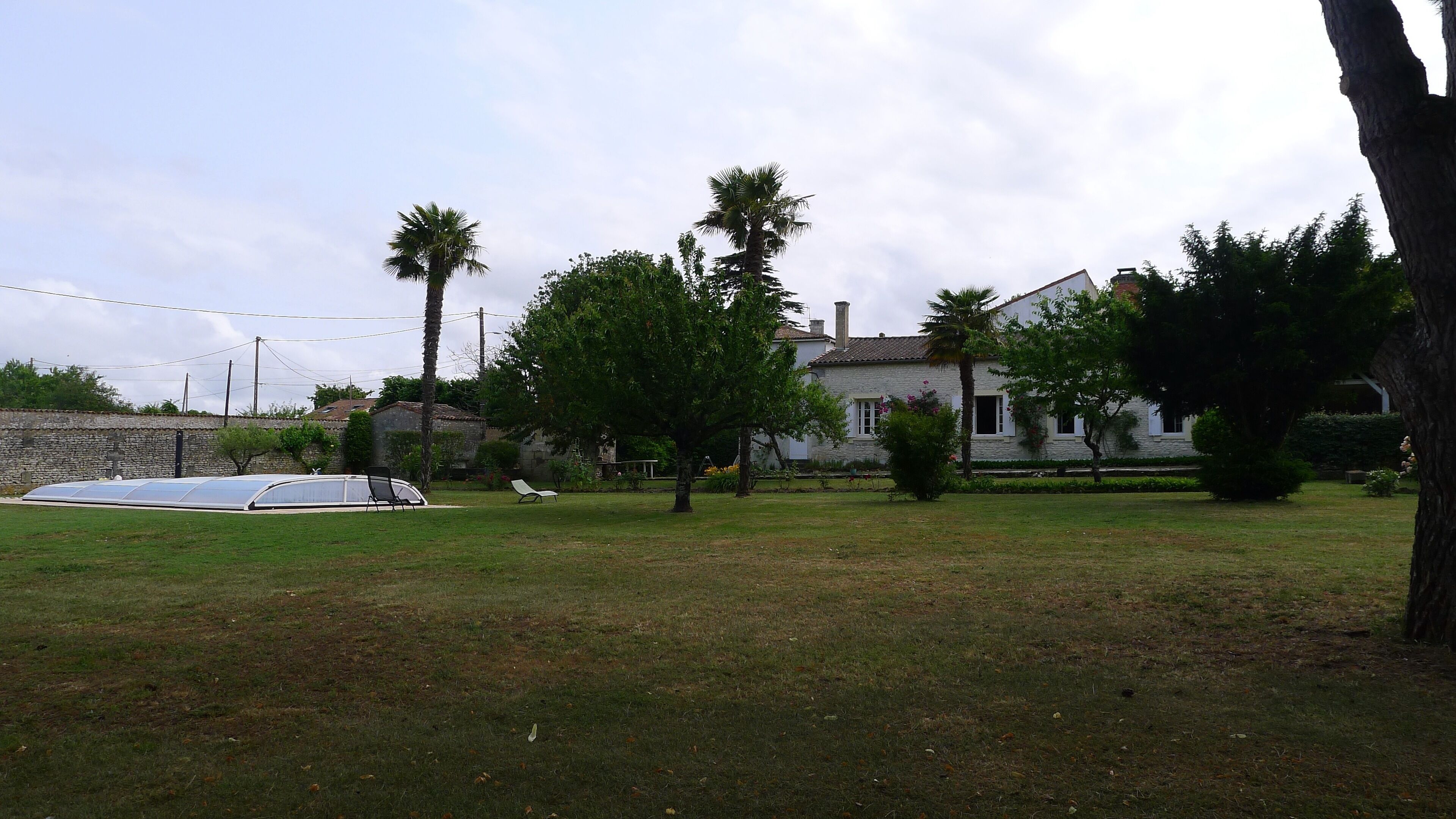 Una casa amb un mur de pedra, una piscina i un jardí amb arbres.