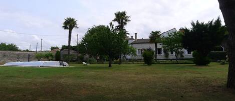Una casa amb un mur de pedra, una piscina i un jardí amb arbres.