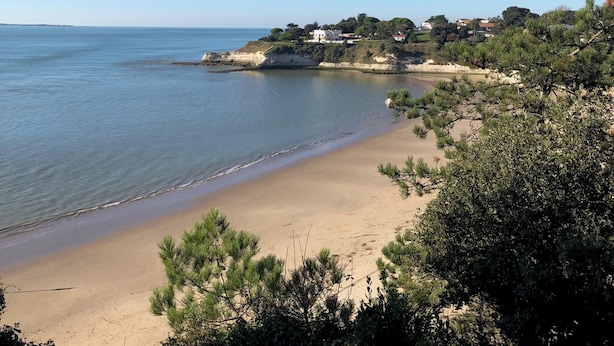 Et kystlandskab med en sandstrand, klarblå himmel og en lille bebyggelse med huse på en skråning.
