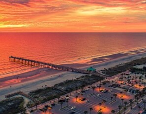 A coastal view with a pier extending into the water, a parking lot, and a building with a green roof. - Jacksonville Beach for 6 Bike Fenced Private (Jacksonville Beach)