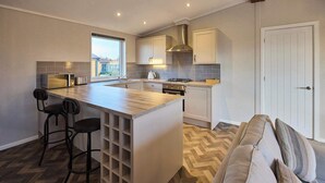 A modern kitchen with a central island, bar stools, a built-in oven, and a window. - Host & Stay | Hazelwood Deluxe Lodge (Low Gate)