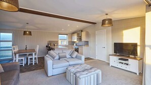 A modern living room with a sofa, ottoman, and a TV stand with gaming consoles. - Host & Stay | Hazelwood Deluxe Lodge (Low Gate)